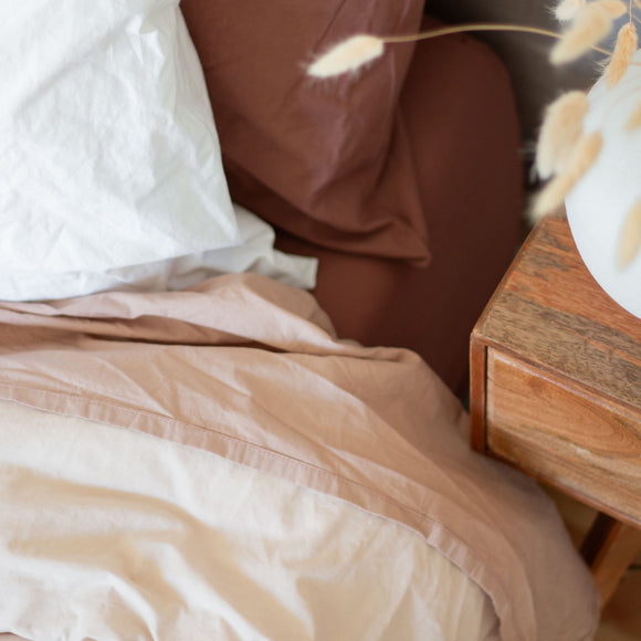 Close-up of a bed with brown and white bedding, and a wooden nightstand.