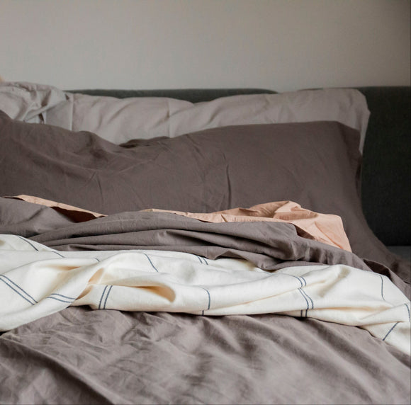 Bed with gray bedding and a blanket, featuring a neutral color palette.