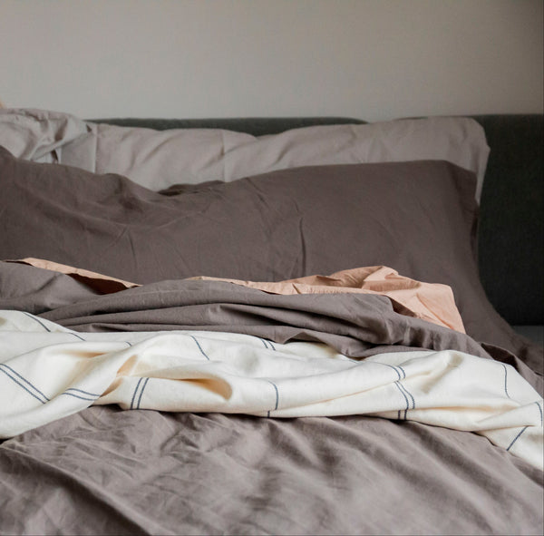 Bed with gray bedding and a blanket, featuring a neutral color palette.